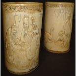 A pair of carved ivory brush pots, each set with Greek key design border to the top,