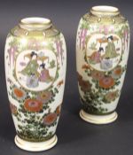 A pair of Japanese Satsuma vases with panels of figures in interior settings amongst trailing