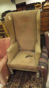 A wing back armchair in oatmeal upholstery raised on turned legs to brass caps and castors stamped