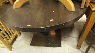 A modern circular dining table, the top of dark colouring,