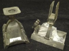 An Arts and Crafts pewter candlestick and matchbox holder, each supported on an arching twin column,