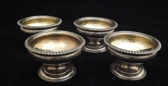 A set of four George III silver salts of circular pedestal form with gadrooned rims and raised on