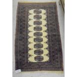 A Bokhara rug, the central panel set with nine repeating elephant foot medallions on a cream ground,