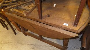 A pine drop-leaf circular table, raised on turned and ringed legs united by a stretcher,