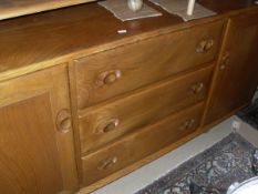 A light elm Ercol sideboard with three central drawers flanked by cupboard doors
