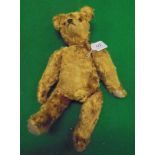 A gold plush wood wool filled bear in the manner of Steiff with glass eyes and worn felt pads