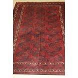 An Afghan carpet, the central red ground with repeating elephant foot medallions in dark blue,