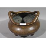 A Chinese bronze censer of heavy cast form with loop handles on three short feet,