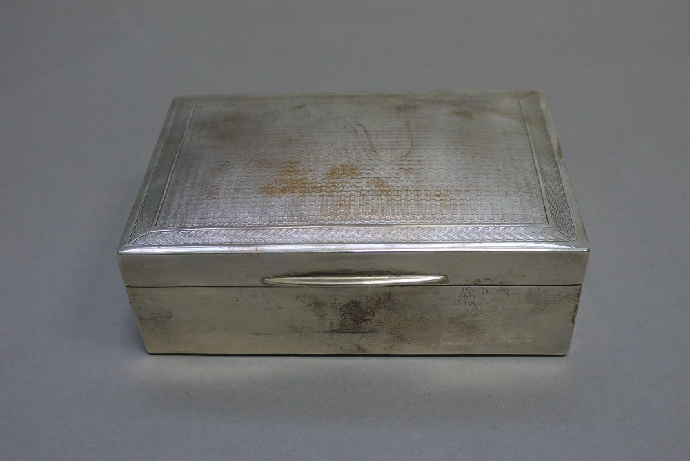 A silver cigarette box of plain rectangular form, with engine turned decoration to cover,