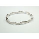 NINE CARAT WHITE GOLD BANGLE of wavy form and with safety clasp, approximately 7.