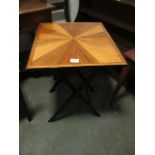 A FOLDING TABLE with segmented top raised on ebonised folding stand