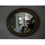 A GILT FRAMED OVAL WALL MOUNTED MIRROR with gadrooned rim and beaded border with bevelled plate