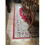 A WOOL RUG the cream ground decorated with a central red panel filled with an oversized flowerhead