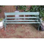 A GREEN PAINTED AND CAST IRON GARDEN BENCH WITH SLAT BACK AND SEATS on foliate shaped side supports