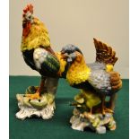 A pair of Bavarian porcelain models of a cockerel and a hen with chicks, standing on a green