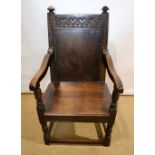 An oak wainscoat chair, with carved crest and foliage carved side supports to the plain panelled