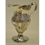 A George III style inverted pear shape cream jug, with chased foliage and a beaded rim, a leaf