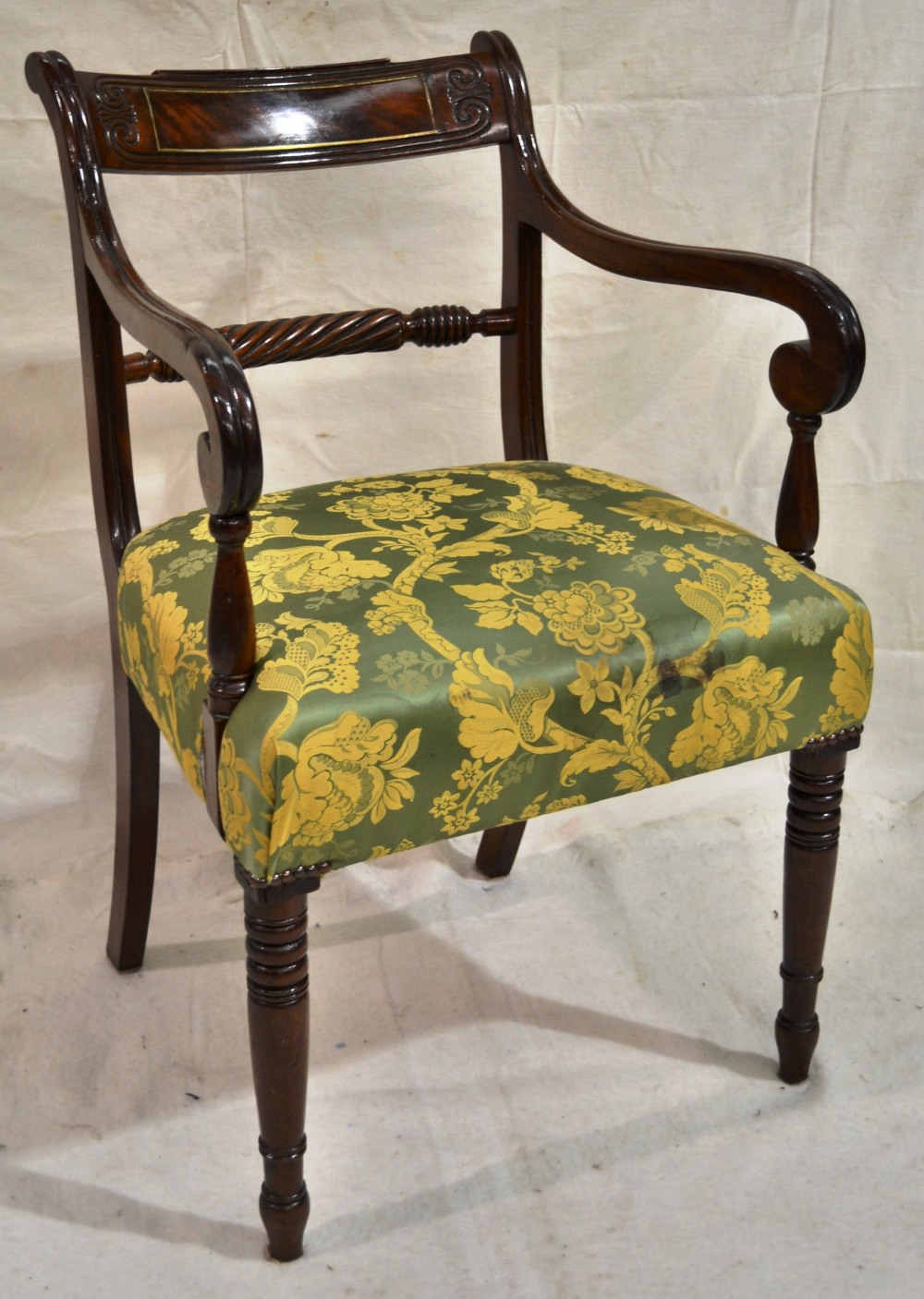 A Regency mahogany elbow chair, the curved rope rail back with a scroll leaf carved crest, the