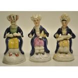 Three early nineteenth century Staffordshire seated Turk candle extinguishers, two holding musical