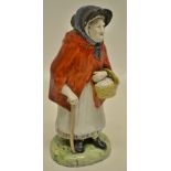 An early nineteenth century Prattware figure of an Old Woman, wearing a red cape and a black bonnet,