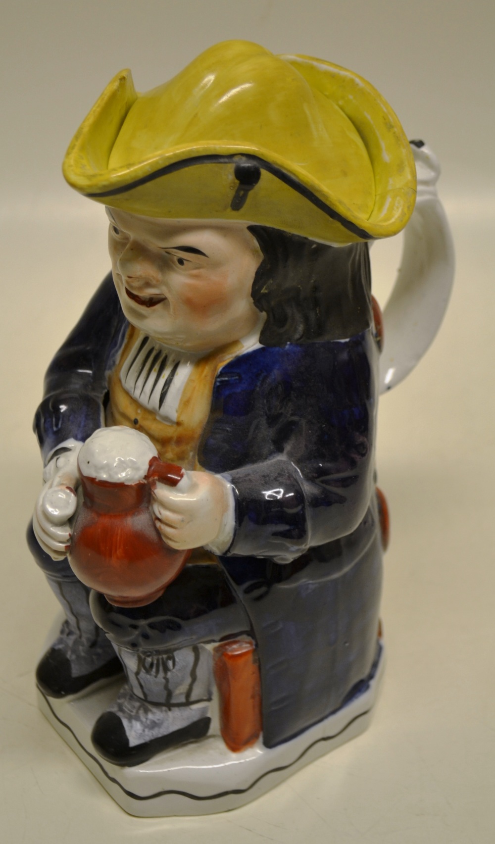 A Victorian Staffordshire toby jug with yellow tricorn hat seated on a chair, holding a jug of ale