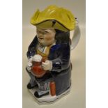 A Victorian Staffordshire toby jug with yellow tricorn hat seated on a chair, holding a jug of ale
