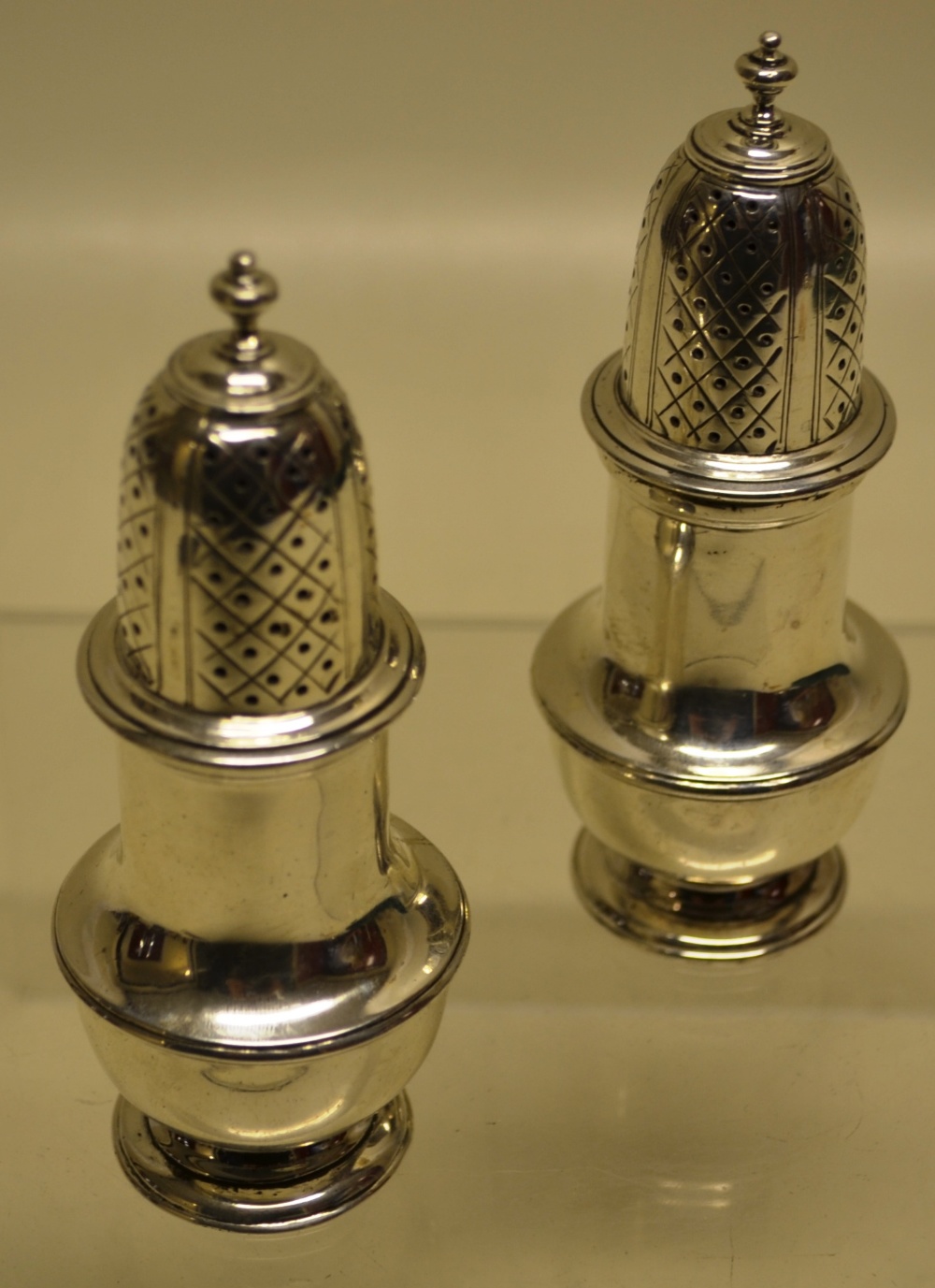 A pair of silver baluster peppers in George II style, with pierced covers, on a cast moulded foot.