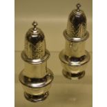 A pair of silver baluster peppers in George II style, with pierced covers, on a cast moulded foot.