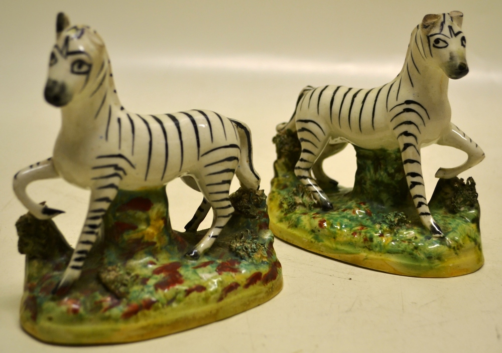 A pair of nineteenth century Staffordshire zebras, (ears chipped), standing on a green splash