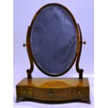 A George III mahogany veneered oval swing toilet mirror, with a later bevelled glass, on scroll