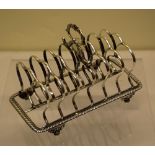 A George IV silver toast rack, with seven scrolling wire-work divisions and a central acanthus
