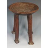 An African tribal stool the circular dished top on four rudimentary feet with carved bases,