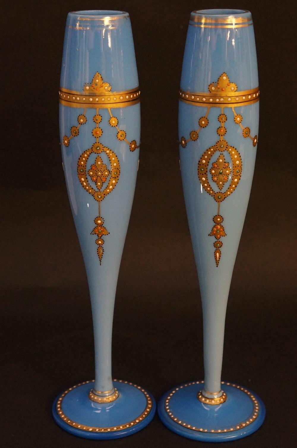 A pair of slender opaque blue glass vases, gilded pendant drapes embellished with white,