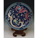 A Chinese circular charger decorated with yellow and pink dragons on a stylised blue cloud ground,