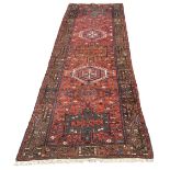 A Persian Heriz runner, seven geometric medallions of various colours on red ground,