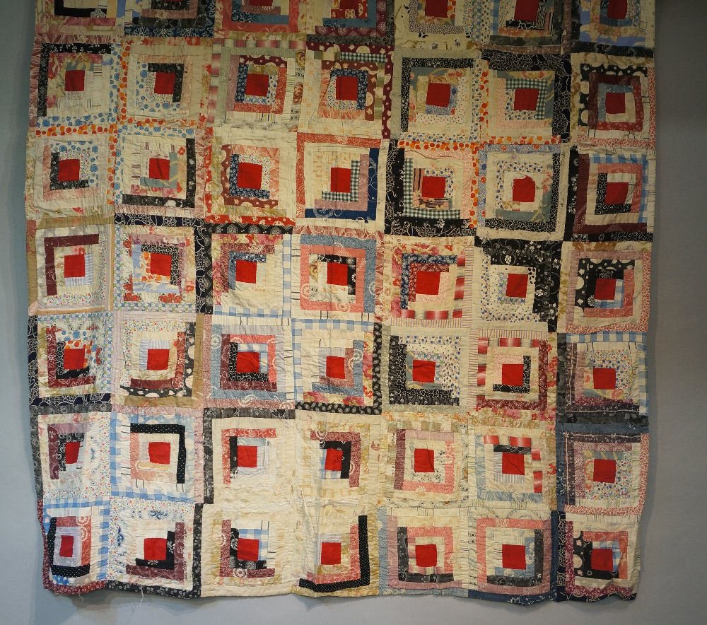 An early to mid 20th Century log cabin patchwork quilt made up of seven by ten multi coloured