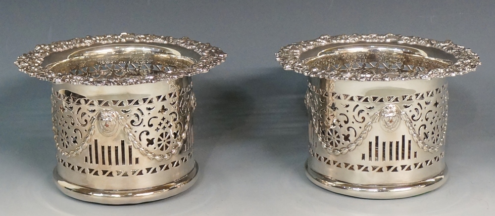 A pair of silver plated bottle coasters, the bodies pierced with scrolls, bars and crosslets,