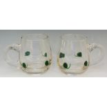 A pair of glass mugs or tankards, the plain bodies with applied green commas and applied handles,