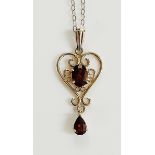 A 9ct gold scrolling heart shaped garnet set pendant and drop on a fine link necklace