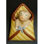 A late 19th Century wall pocket modelled as a dog contained in a woven ribbon tied wall basket,