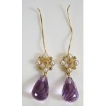 A pair of amethyst earrings with pear shaped amethyst faceted pendants beneath a stylised