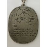 A pewter oval pendant engraved with a child like image above "Anxieties Yield At A Negative Rate,