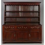 An early Georgian oak dresser with panelled delft rack and three drawers over cupboard base banded
