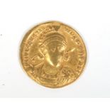 A Roman gold Solidus coin with helmeted bust facing holding a spear and shield,