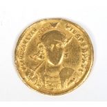 A Roman gold Solidus coin with helmeted bust facing holding a spear and shield,