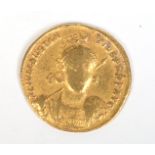 A Roman gold Solidus coin with helmeted bust facing holding a spear and shield,