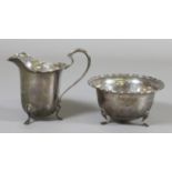 A George VI silver sugar bowl and cream jug each with scalloped rim and raised on three cabriole