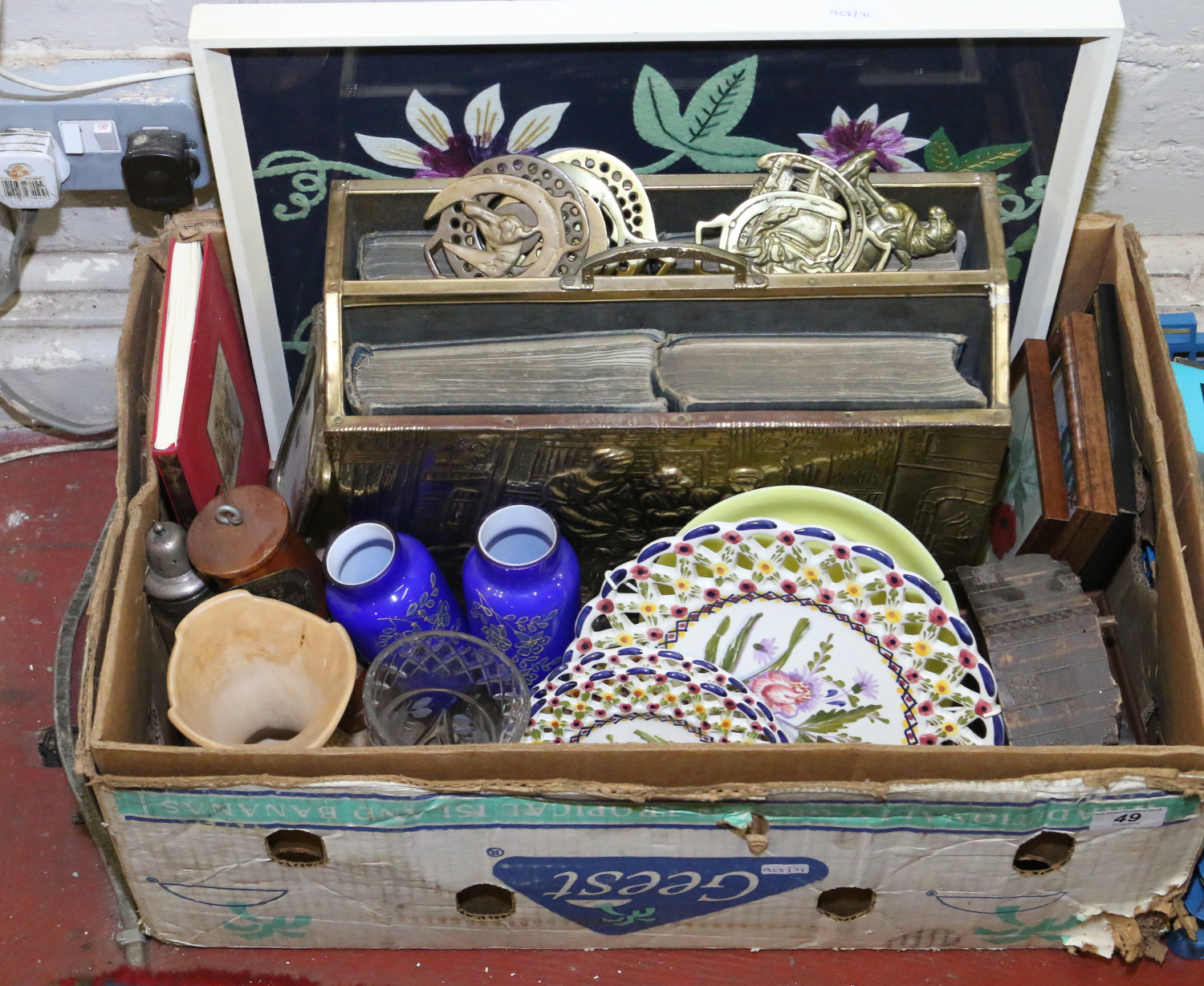 A box of various collectables to include a framed embroidery and a brass magazine rack along with