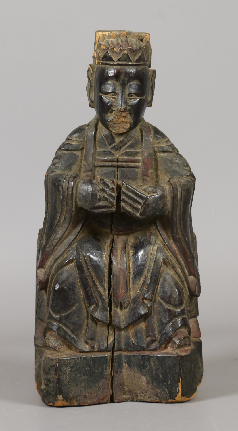 An antique Chinese carved wooden figure of a deity seated upon a throne.