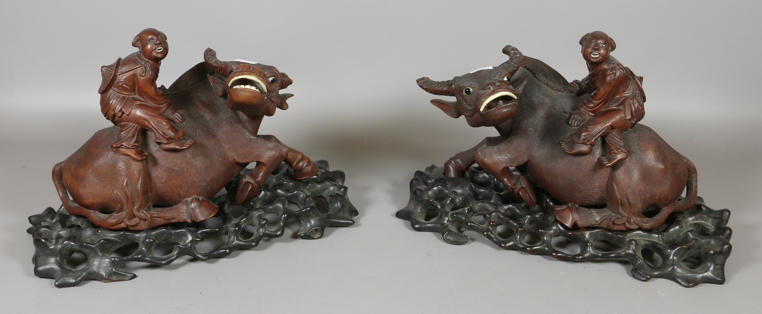 A pair of Chinese carved hardwood figures of oxen and riders raised on stands (AF).